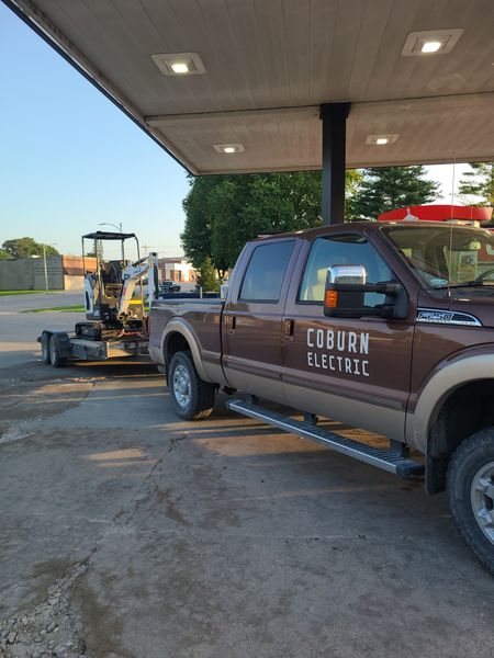 Coburn Electric branded pickup truck towing a mini excavator on a trailer