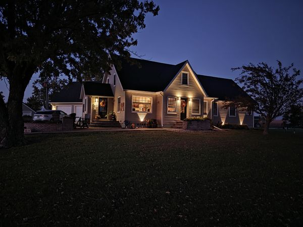 Home at dusk with exterior uplighting along the siding and lit porch lights