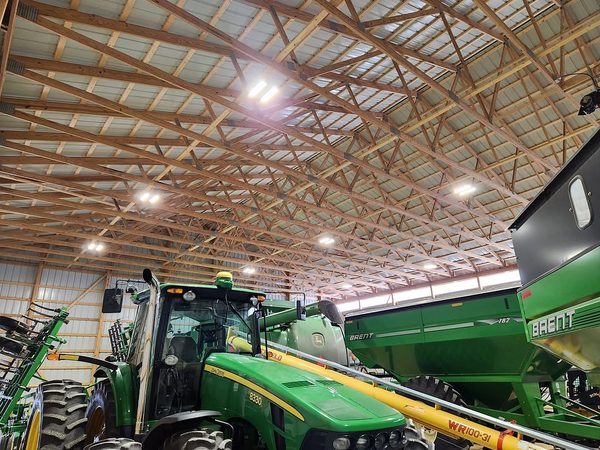 Machine shed with LED high-bay lights over a John Deere tractor and grain carts