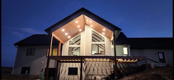 New home at dusk with recessed soffit lights in the wood ceiling of a tall gabled porch